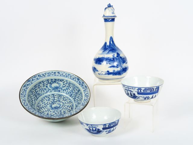 Bouteille en céramique bleu sur fond crème, décor de paysage lacustre.