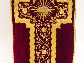 Chasuble en velours rouge. Au dos, croix de galon or décorée d'entrela