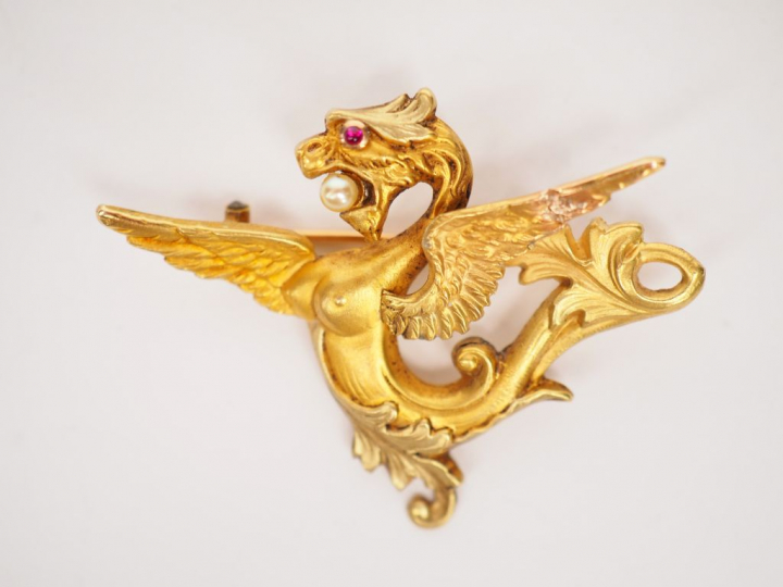 Broche en or jaune en forme de chimère tenant dans sa gueule une perle