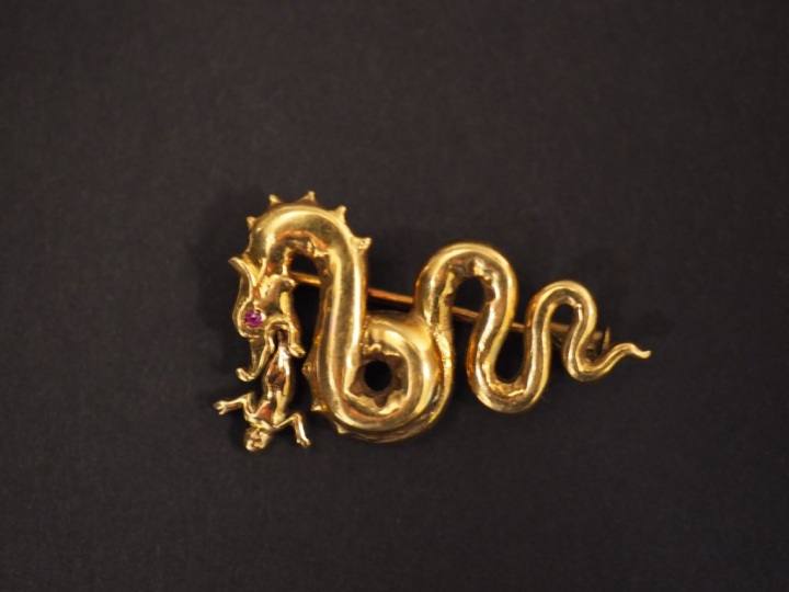 Broche en or jaune en forme de dragon crachant un petit enfant.  L'œil