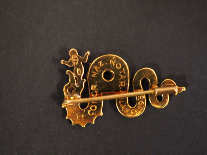 Broche en or jaune en forme de dragon crachant un petit enfant.  L'œil