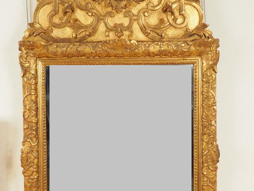 Glace XVIIIème en bois et stuc sculpté doré.  Fronton à décor de masca