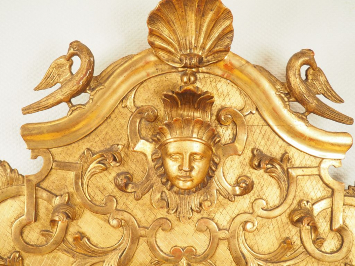 Glace XVIIIème en bois et stuc sculpté doré.  Fronton à décor de masca