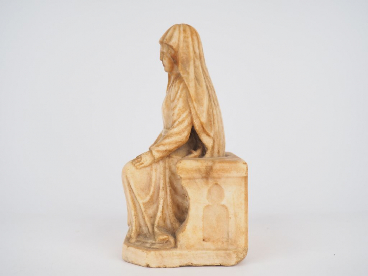Vierge en albâtre sculpté en ronde-bosse. Assise sur un banc-trône orn