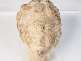 Vente aux enchères Tête en pierre calcaire sculptée aux yeux fendus et à la chevelure bou