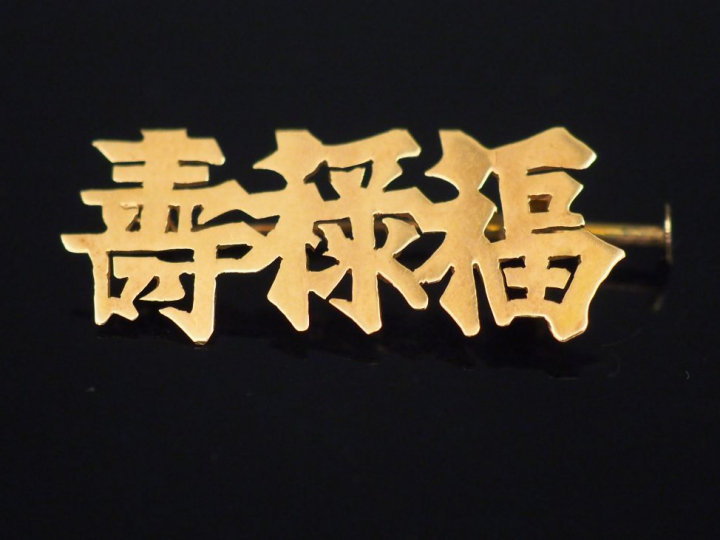 	Broche en or jaune, à décor de caractères asiatiques. Long. 3,5 cm Po