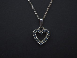 Vente aux enchères 	Pendentif en or blanc en forme de coeur, serti de petits saphirs. On 