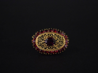 Vente aux enchères 	Broche ovale en or jaune et grenats, à décor ajouré et filigrané d’ar