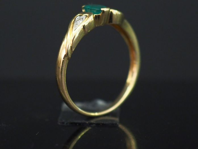 Bague en or jaune, sertie en son centre d’une émeraude épaulée de deux