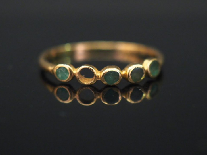Petite bague en or jaune, sertie d’une ligne de quatre pierres vertes.