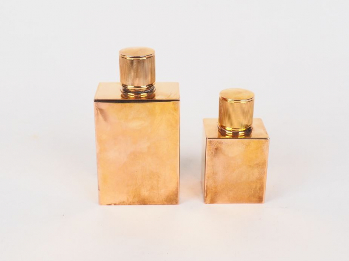 HERMES.  Deux différents flacons en métal doré. Signés. H. 11 cm et 8 