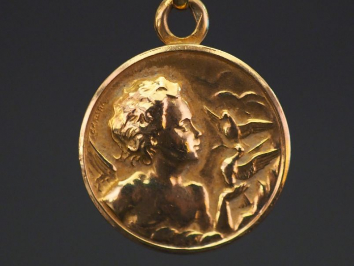 Médaille religieuse en or jaune, figurant un angelot aux oiseaux. Diam