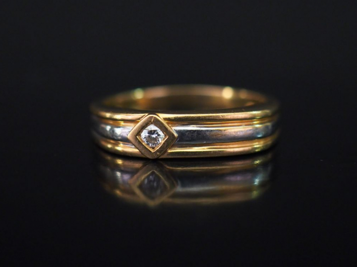 Bague de forme stylisée trois tons d'or, sertie d'un petit diamant.  T