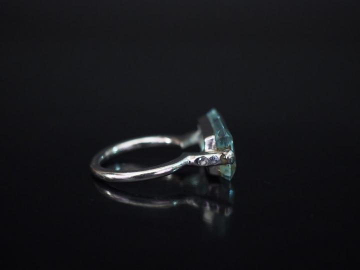 Bague en or blanc, sertie en son centre d'une pierre bleu ciel épaulée