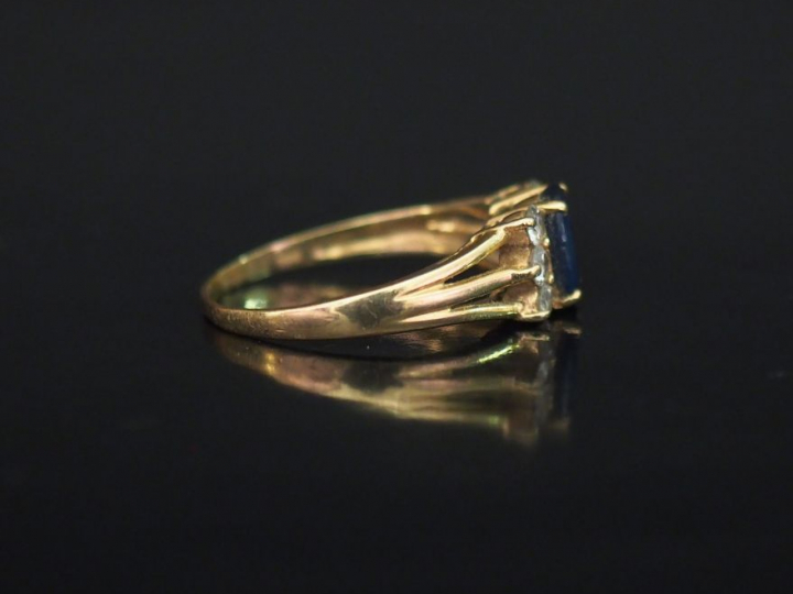 Bague en or jaune 14k, sertie en son centre d'une pierre bleue épaulée