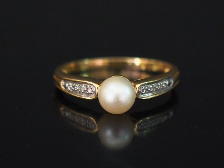 Bague en or jaune, sertie en son centre d'une perle blanche épaulée de