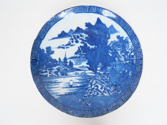 Vente aux enchères Plat en porcelaine à décor au pochoir en camaïeu de bleu d'un paysage 