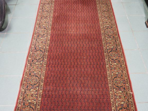 Grand tapis galerie à fond rouge. Dim. 6,80 x 100 cm (petites usures)