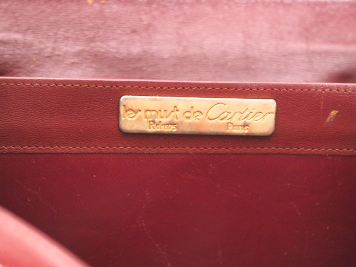 CARTIER, Must Sac bandoulière en cuir bordeaux.  Fermeture à rabat et 