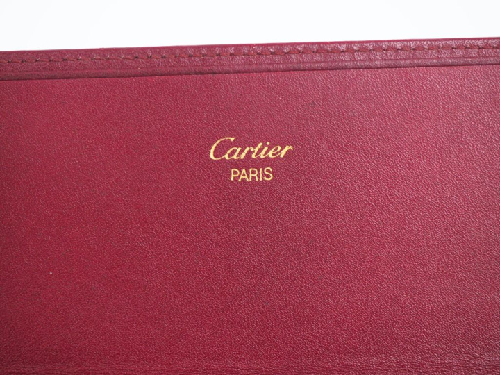 CARTIER,  Porte-feuilles en cuir bordeaux.  Signé.  10 x 19 cm (petite