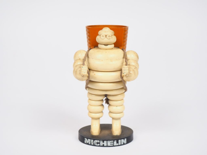 MICHELIN.  Porte crayon Bibendum vendangeur en plastique et métal. H. 