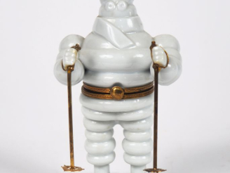 Vente aux enchères MICHELIN.  Bibendum skieur, boîte en porcelaine de Limoges. H. 14 cm.