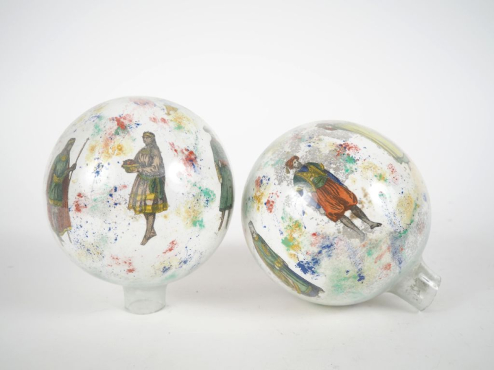 2 boules porte-perruque en verre églomisé à décor de personnages. H. 1