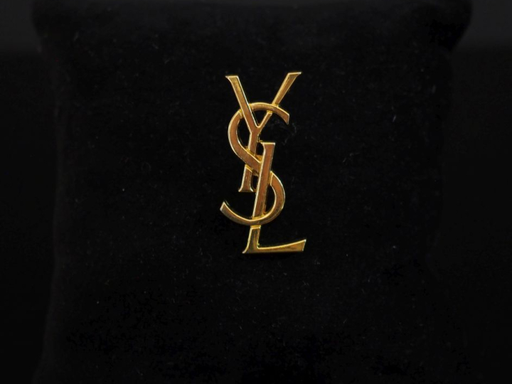 YVES SAINT LAURENT Pin's en métal doré figurant le monogramme de la ma