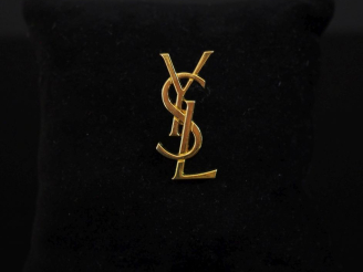 Vente aux enchères YVES SAINT LAURENT Pin's en métal doré figurant le monogramme de la ma