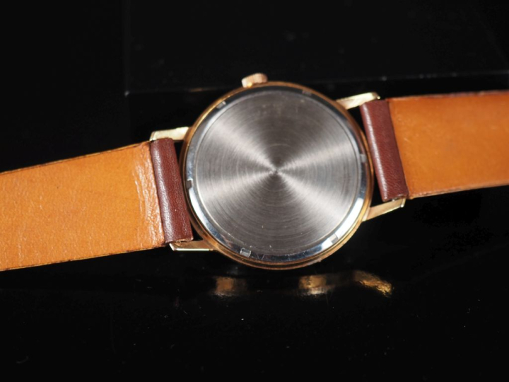 PAX Montre bracelet en métal doré.  Cadran rond à fond crème, index bâ