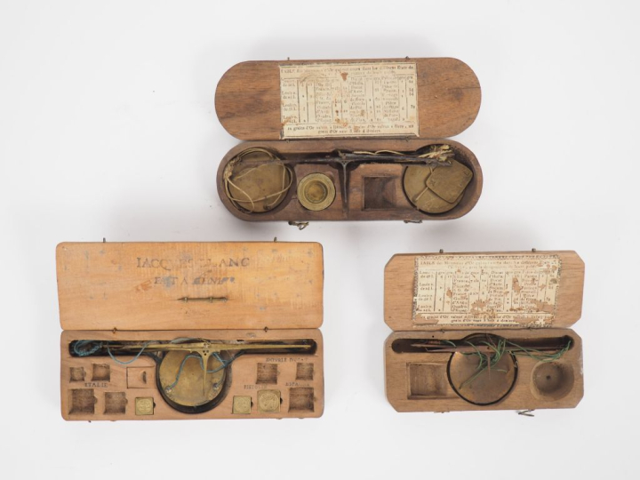 Trois différents trébuchets anciens dans leurs coffrets. (Eléments man