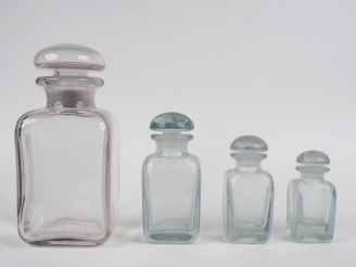 Vente aux enchères HERMES Garniture en verre comprenant quatre flacons et leur bouchon.  
