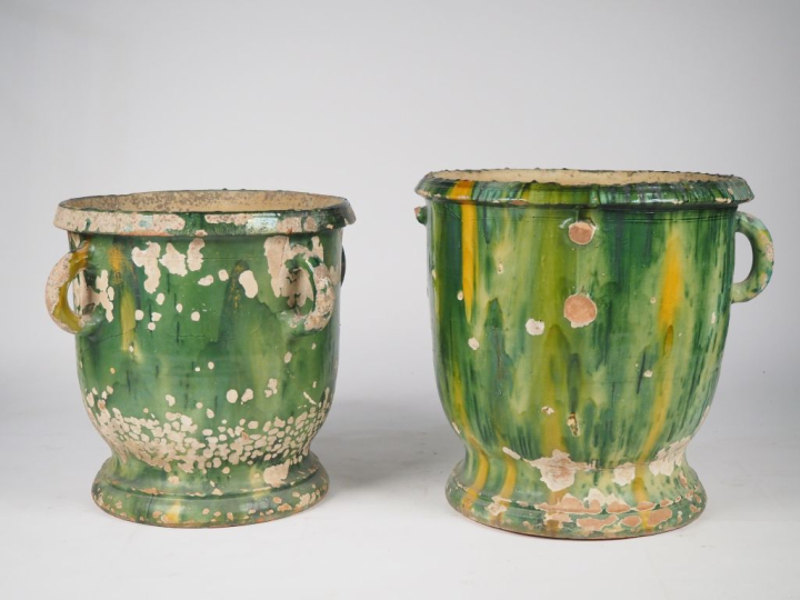 2 différents pots en terre vernissée verte nuancée de jaune, sur piédo