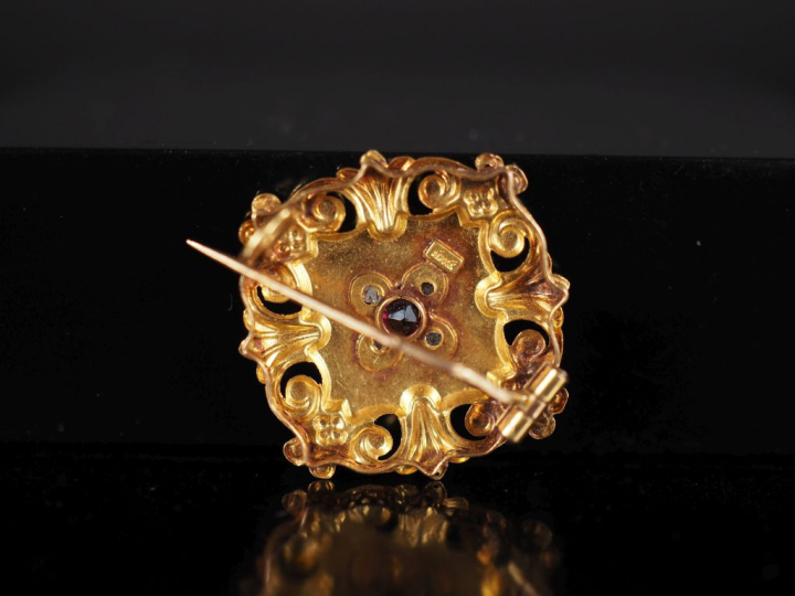 Petite broche en or 750, à décor ajouré de rinceaux et sertie en son c